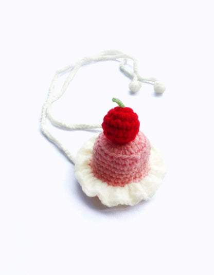close-up of hand-knitted cherry cake pet birthday hat with red cherry detail and soft yarn texture