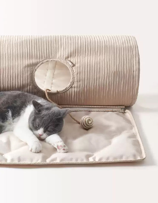 A kitten resting beside a tunnel on a cooling pet mat, enjoying a calm summer nap
